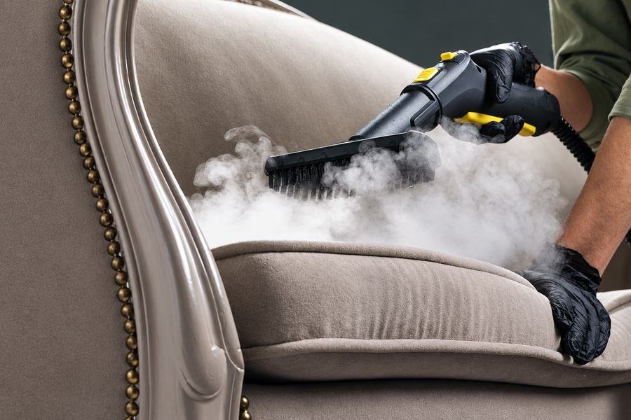 Steam cleaning head being worked across the seat of an upholstered armchair